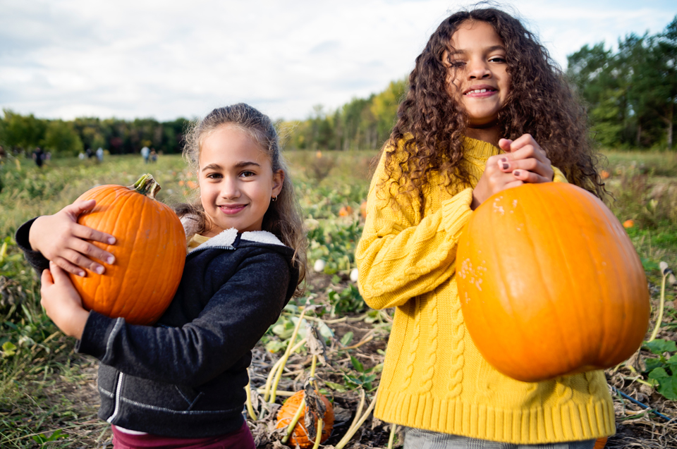 Two girls holding pumpkins at the pumpkin patch.